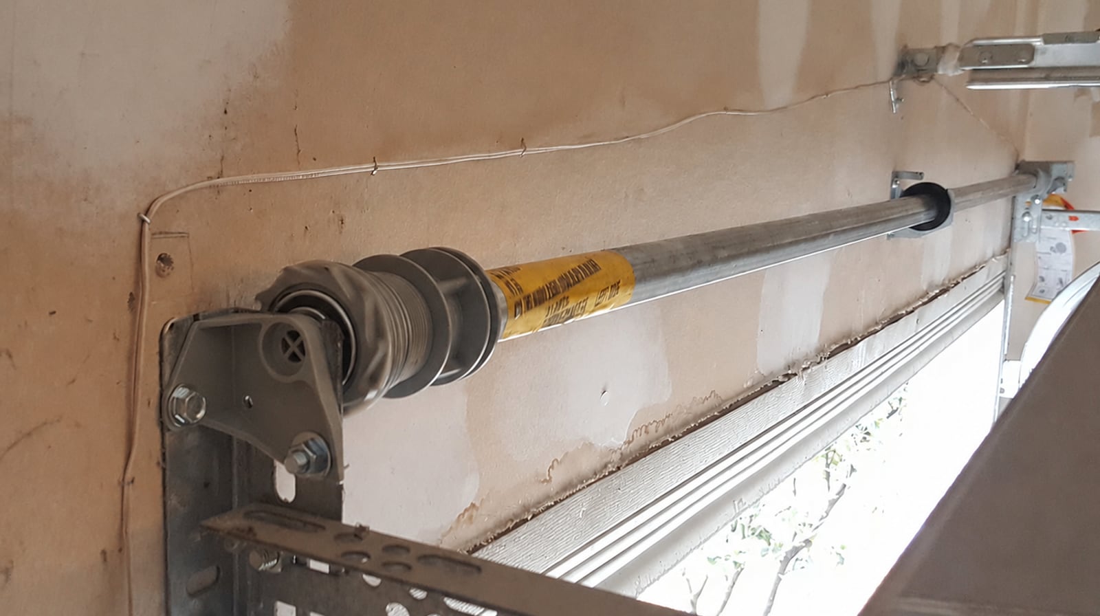 A wound torsion-spring tube above a Coquitlam garage with the original yellow Wayne Dalton TorqueMaster warning label still attached.