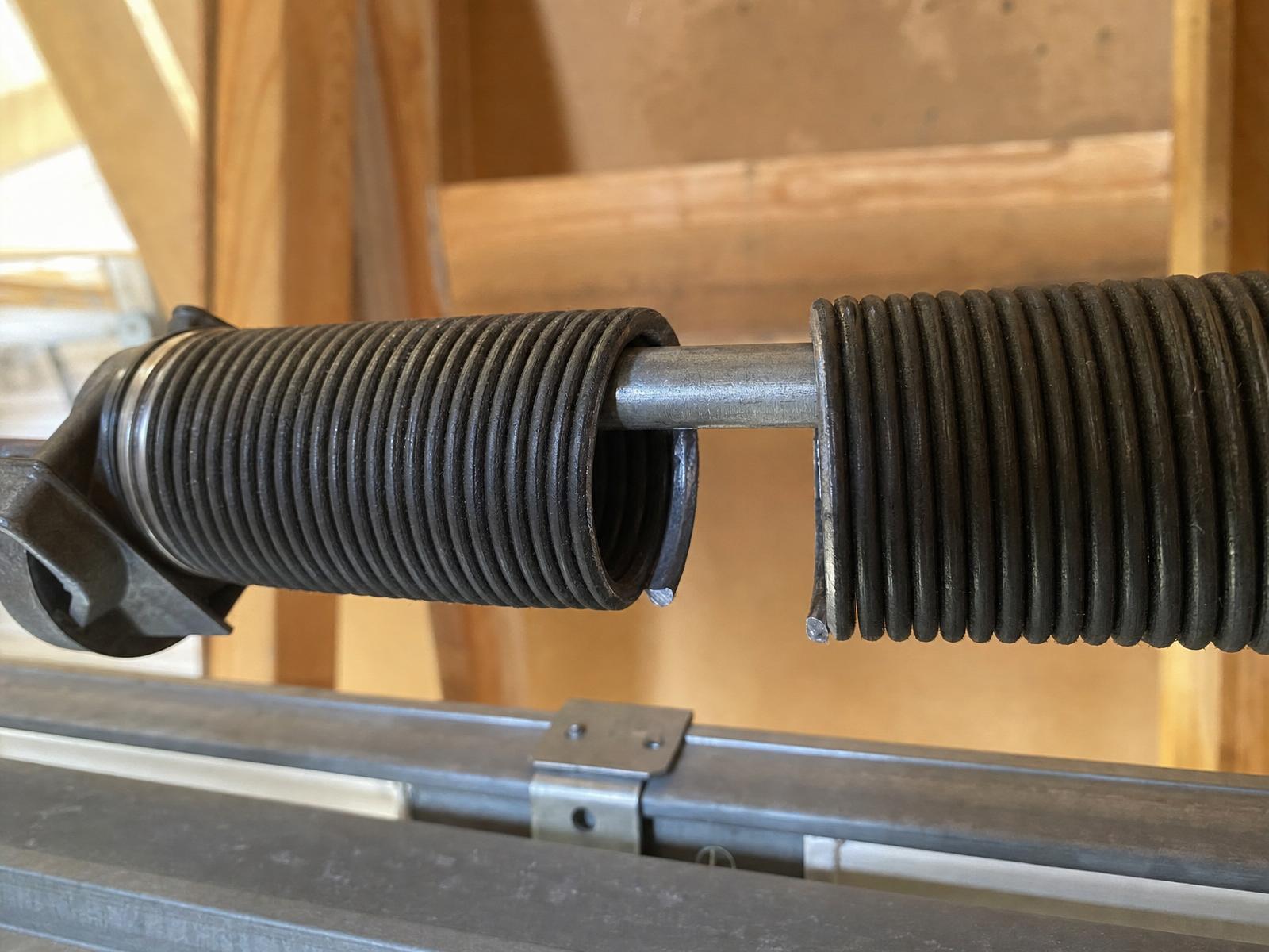 Close-up of a broken residential garage door torsion spring with a visible gap in the coil
