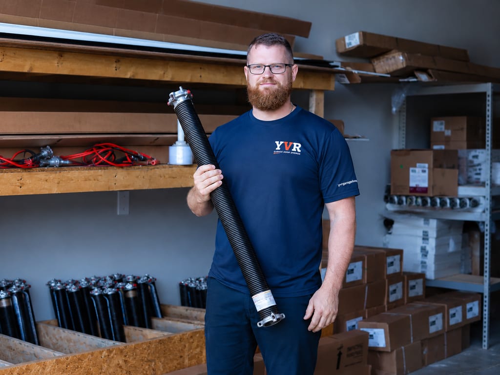 A YVR Garage Door Springs technician in the shop holding a single black oil-tempered residential torsion spring.
